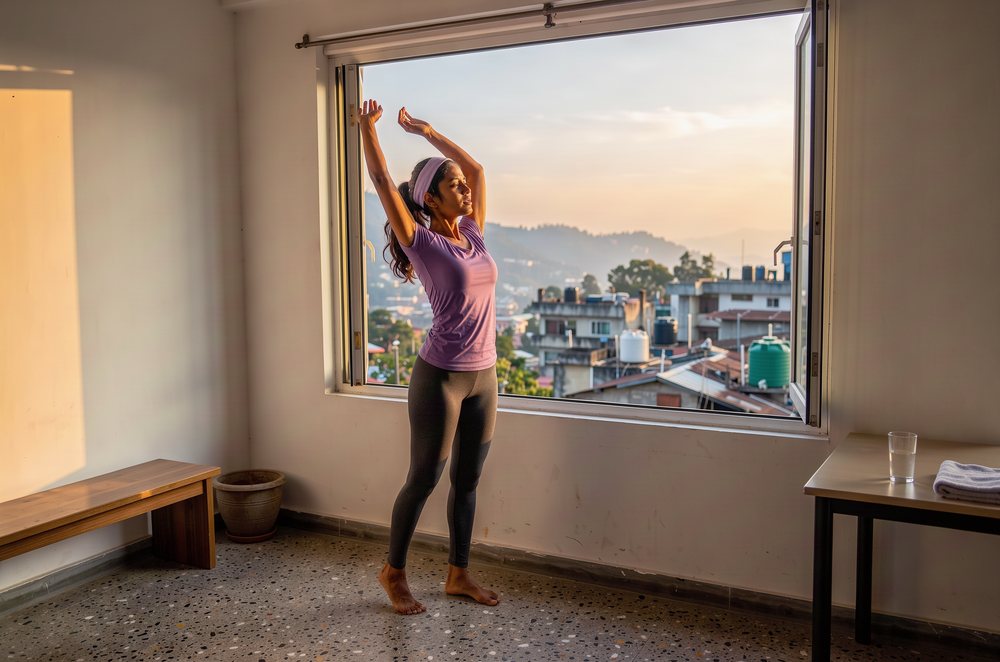 A woman stretching by an open window at sunrise.